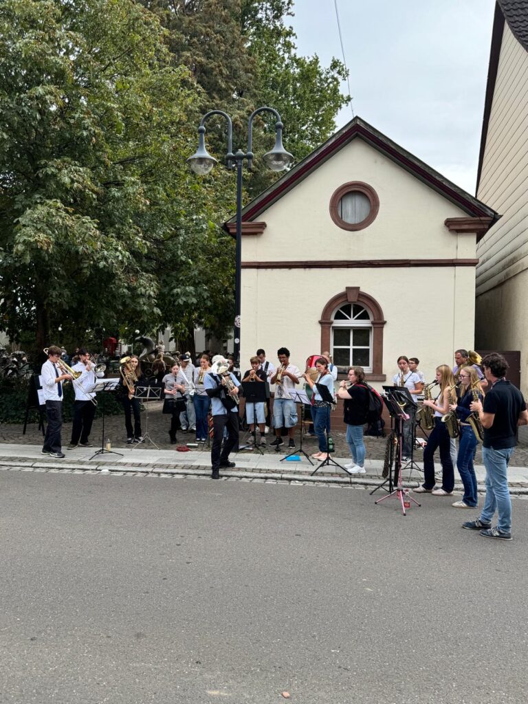 Die United Concert Band spielt vor einem kleinen Haus an der Hauptstraße in Herxheim.